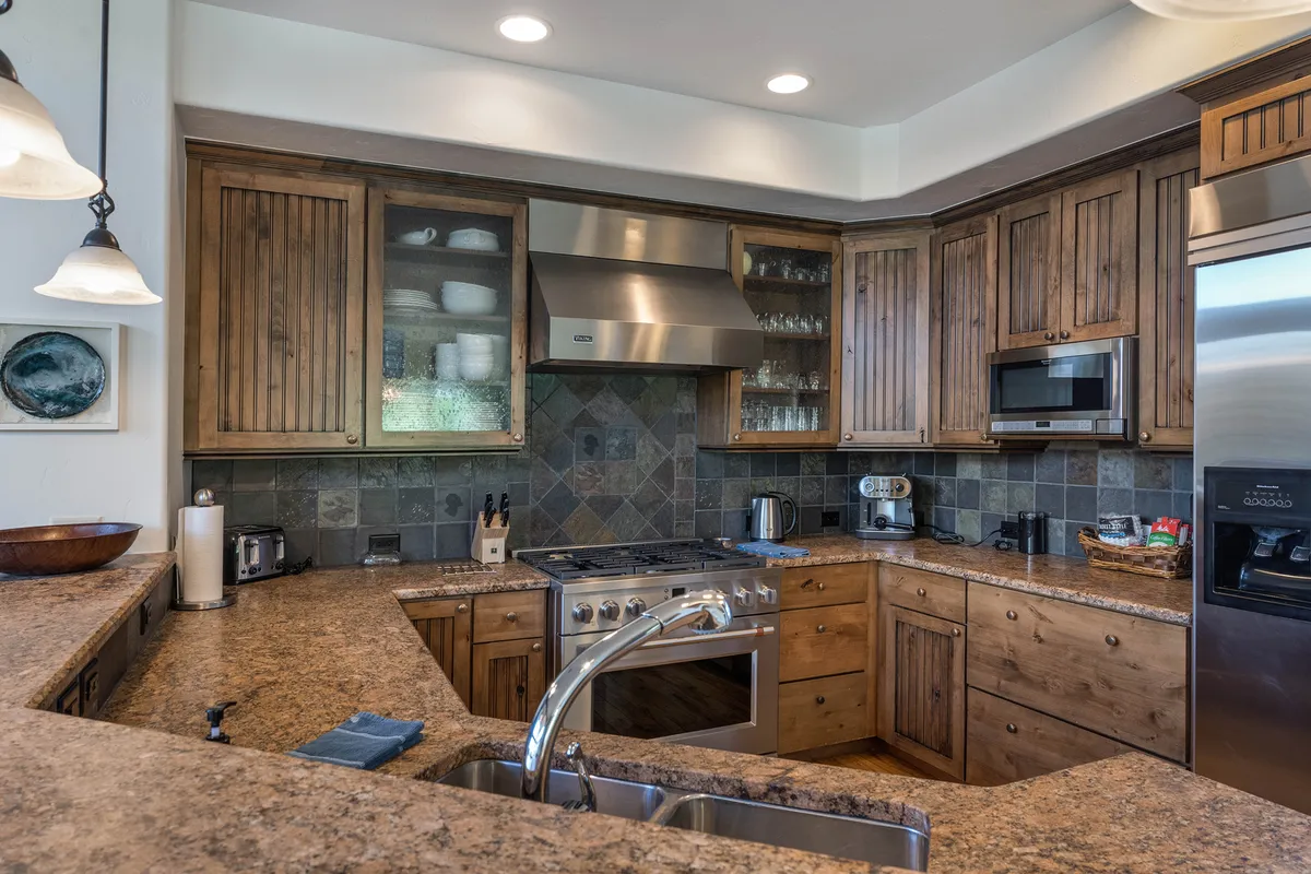 A spacious, gourmet kitchen with granite countertops, warm wooden cabinets, stainless steel appliances, and a central island. The scene invites cooking, entertaining, and shared meals, echoing the gathering and group dining focus.