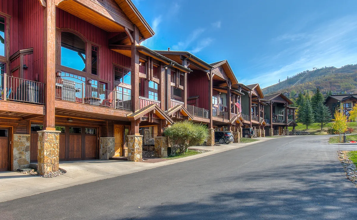 A wide-angle exterior view highlighting Cimarron's rustic wooden architecture, landscaped grounds, balconies, and a dramatic mountain backdrop. The image conveys a welcoming, upscale lodge feel and emphasizes opportunities for outdoor relaxation or morning strolls to the slopes.