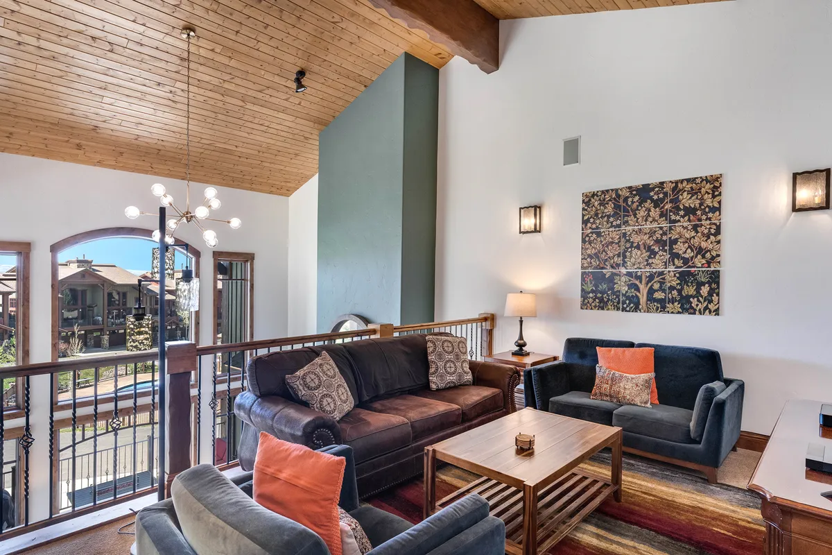 A cozy living room with a plush sofa, coffee table, tasteful artwork, and large windows providing glimpses of the outdoors. The lighting and layout create a welcoming environment ideal for gathering after a day of adventure.