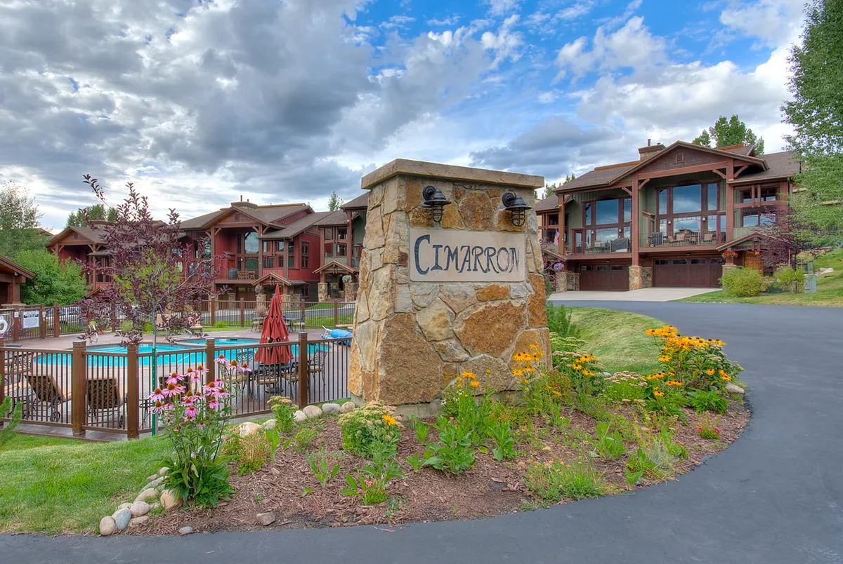 An exterior view of the property featuring the Cimarron stone sign, swimming pool, colorful flower beds, and buildings nestled among greenery. The image conveys a sense of community and connection to the outdoors, with walkways inviting exploration.