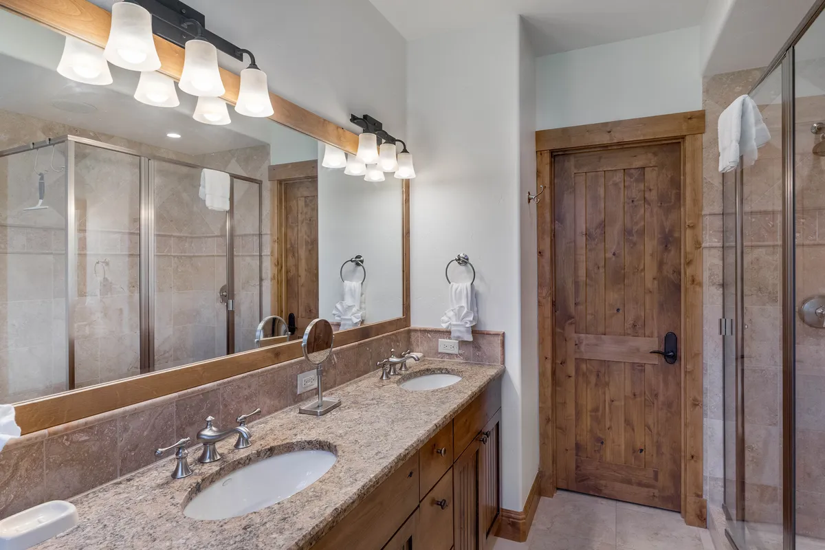 A luxurious bathroom with a double sink vanity, expansive mirror, glass shower enclosure, and wooden accents. The space is organized and calming, offering guests a spa-like experience for morning and evening routines.