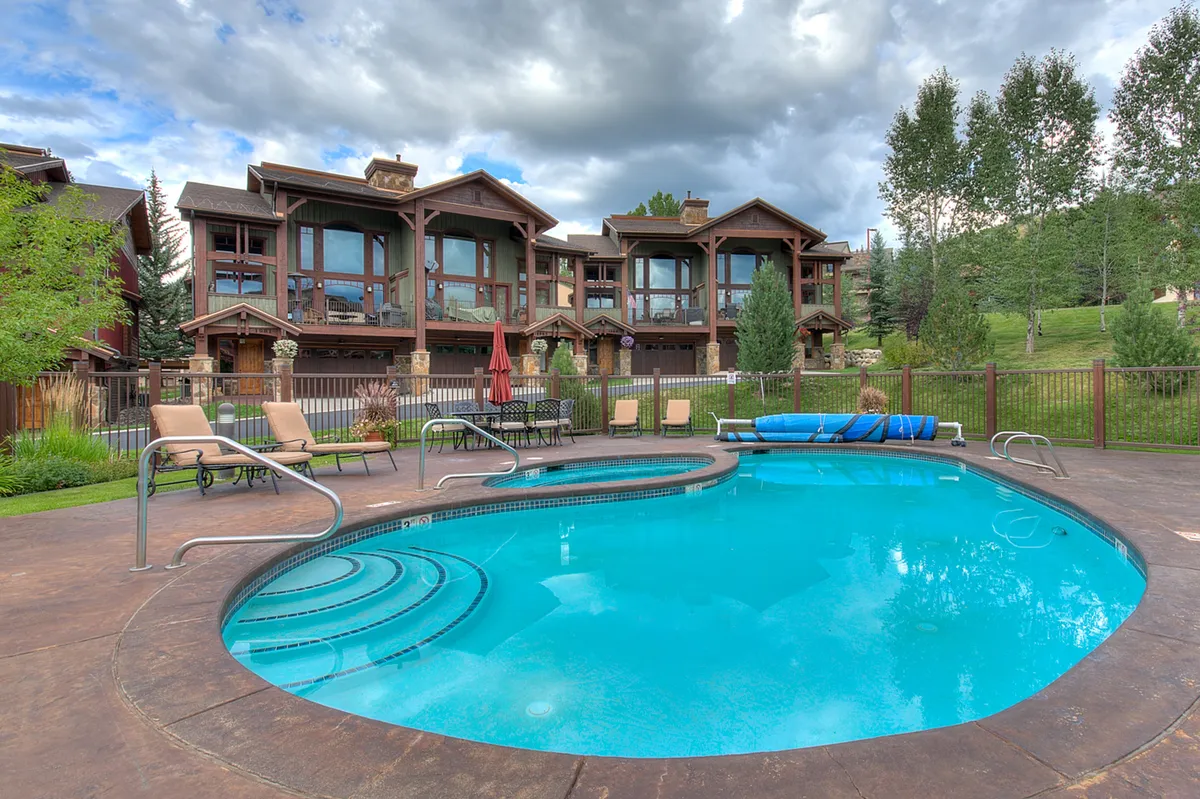 A resort-style outdoor swimming pool surrounded by lounge chairs and mature trees, with the building facade visible in the background. The tranquil poolside setting suggests relaxation and recreation, ideal for unwinding after work or study sessions.