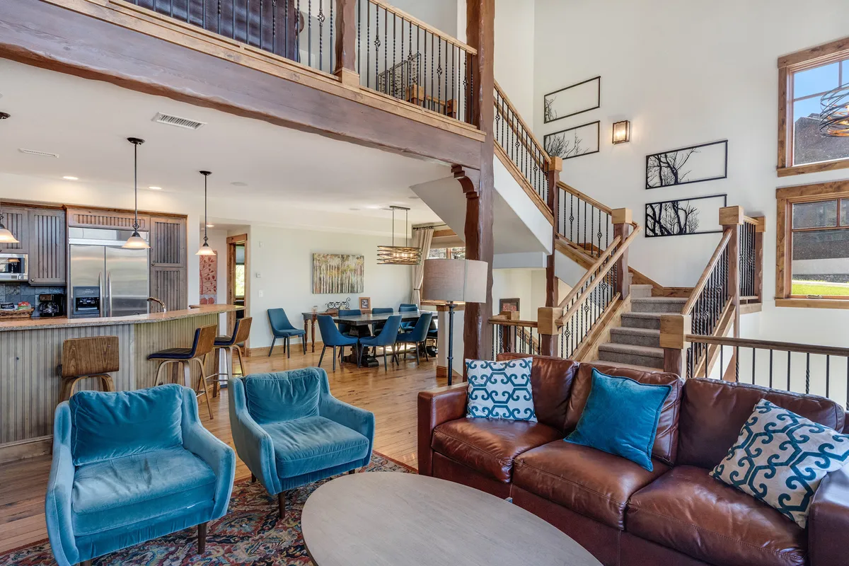 A welcoming interior entry area with a leather sofa, blue accent chairs, and a glimpse of the dining space and staircase. The spacious, organized layout hints at both social gathering spaces and convenient access to the rest of the home.