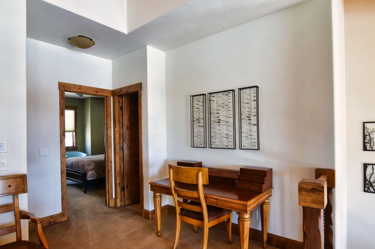 A dedicated workspace with a wooden desk and comfortable chair, accented by decorative wall art. The space is quiet and tucked away, ideal for focused productivity, reading, or creative work sessions. The open doorway hints at a connection to the rest of the home.