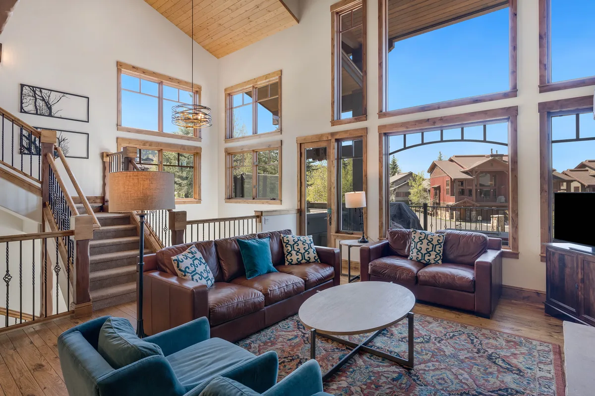 A bright, open loft space featuring large windows that flood the room with natural light. The cozy seating area includes a plush sectional sofa arranged for comfortable group lounging, with a unique lighting fixture overhead adding a modern touch. The ambiance is perfect for movie nights, relaxing, or social gatherings.