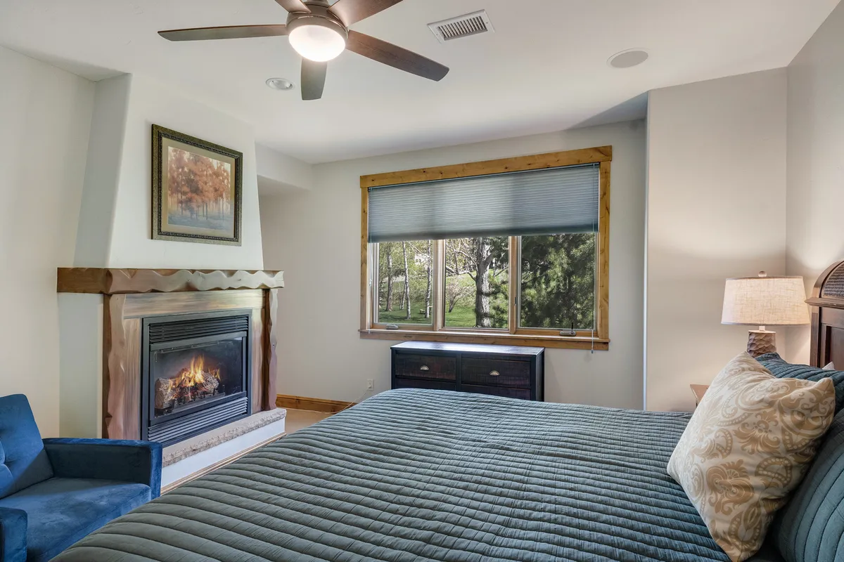 A serene bedroom featuring a plush king bed positioned beside a large window, a cozy fireplace, and calming neutral tones. Natural light streams in, highlighting the relaxing atmosphere and inviting guests to unwind after a long day. The space is uncluttered, with thoughtful touches that suggest luxury and comfort.
